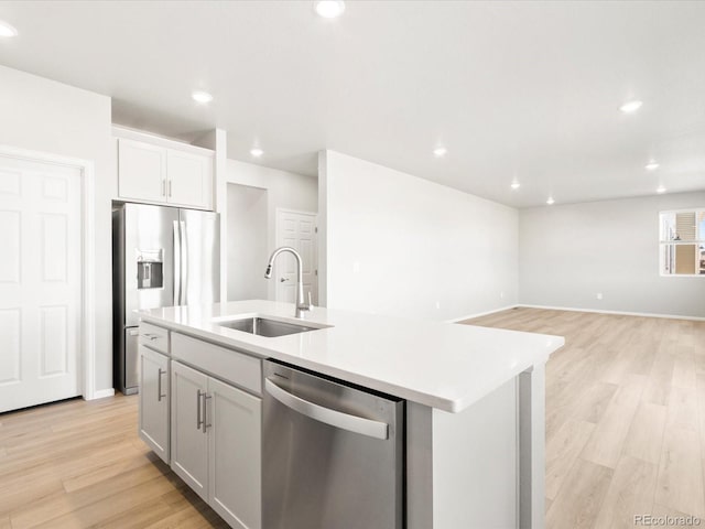 kitchen with light wood finished floors, a kitchen island with sink, a sink, stainless steel appliances, and light countertops