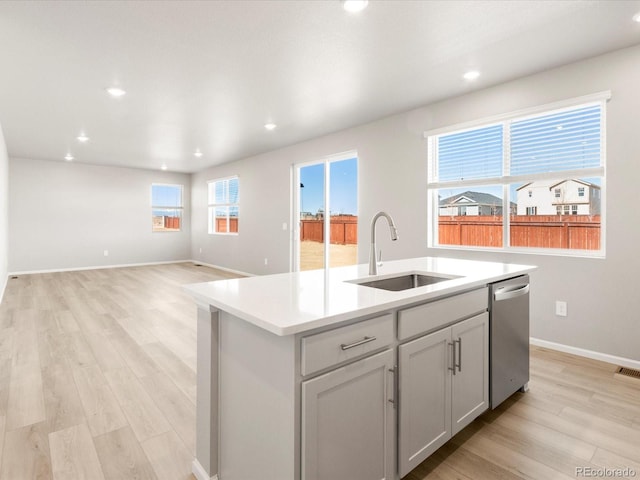 kitchen with light wood-style flooring, an island with sink, a sink, light countertops, and dishwasher