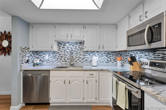 kitchen with appliances with stainless steel finishes, a skylight, sink, and white cabinets