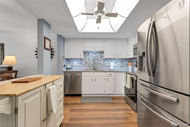 kitchen with light wood-type flooring, a textured ceiling, stainless steel appliances, sink, and white cabinets