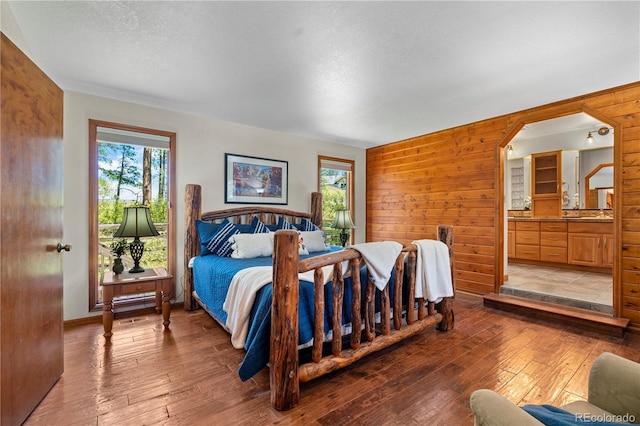 4515 Red Rock Dr, Larkspur, CO 80118 - bedroom featuring light wood-style floors, arched walkways, wood walls, ensuite bath, and a textured ceiling