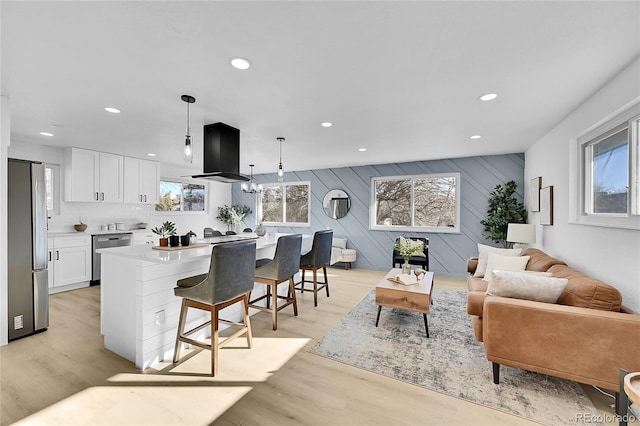 kitchen with appliances with stainless steel finishes, extractor fan, decorative light fixtures, white cabinetry, and light hardwood / wood-style floors