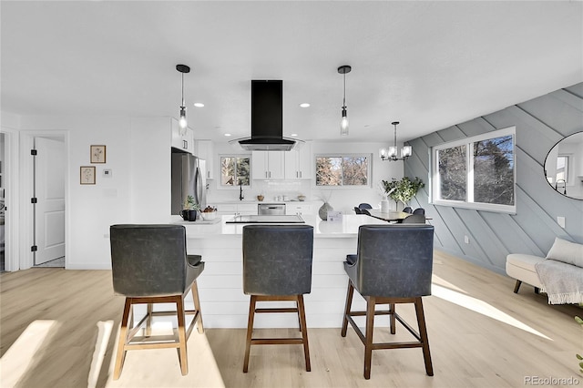 kitchen with island exhaust hood, white cabinets, hanging light fixtures, stainless steel refrigerator, and light hardwood / wood-style flooring