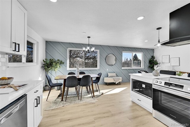 kitchen with decorative light fixtures, extractor fan, appliances with stainless steel finishes, white cabinets, and a chandelier