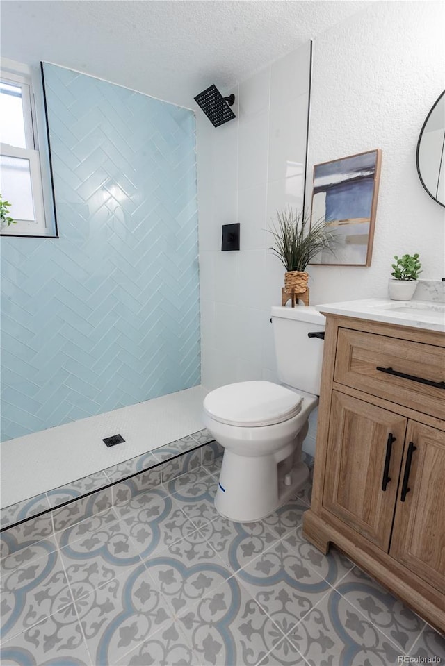 bathroom with a tile shower, vanity, toilet, tile patterned floors, and a textured ceiling