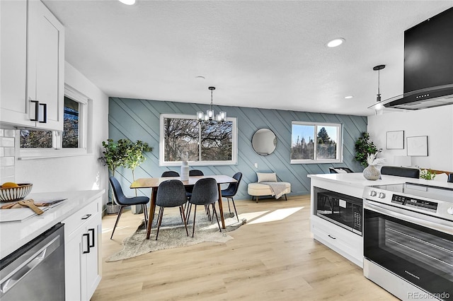 kitchen featuring light hardwood / wood-style flooring, stainless steel appliances, extractor fan, white cabinets, and decorative light fixtures