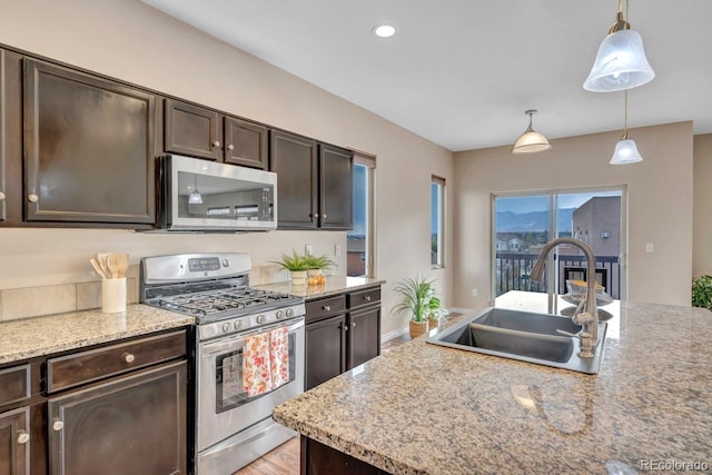 kitchen featuring pendant lighting, sink, appliances with stainless steel finishes, dark brown cabinets, and light stone counters