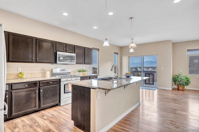 kitchen with a kitchen island with sink, hanging light fixtures, sink, light stone countertops, and appliances with stainless steel finishes