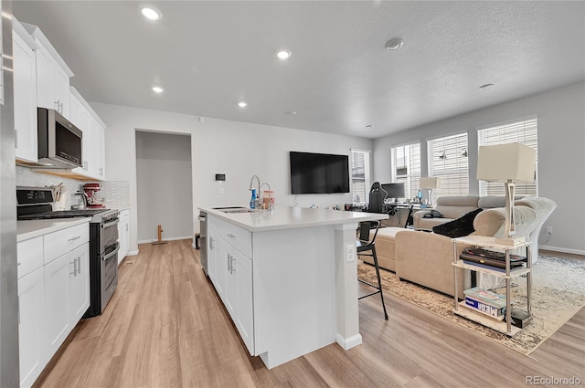 kitchen with a sink, light wood-type flooring, decorative backsplash, stainless steel appliances, and a kitchen island with sink