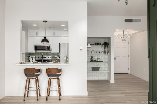 kitchen featuring appliances with stainless steel finishes, backsplash, decorative light fixtures, white cabinets, and light hardwood / wood-style floors