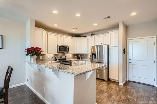 kitchen with kitchen peninsula, white cabinets, dark wood-type flooring, and appliances with stainless steel finishes