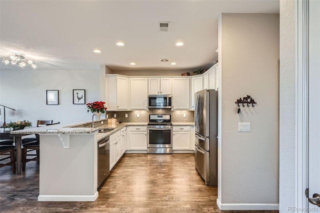 kitchen featuring kitchen peninsula, appliances with stainless steel finishes, a kitchen breakfast bar, light stone counters, and dark wood-type flooring