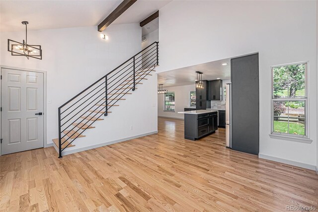 9948 King St, Westminster, CO 80031 - unfurnished living room featuring a chandelier, a towering ceiling, stairs, light wood-type flooring, and beamed ceiling
