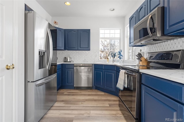 kitchen with blue cabinets, sink, stainless steel appliances, light stone countertops, and light wood-type flooring