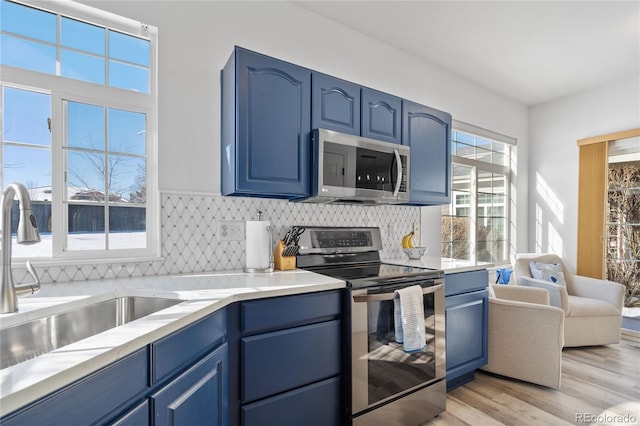 kitchen featuring sink, blue cabinetry, stainless steel appliances, tasteful backsplash, and light hardwood / wood-style floors