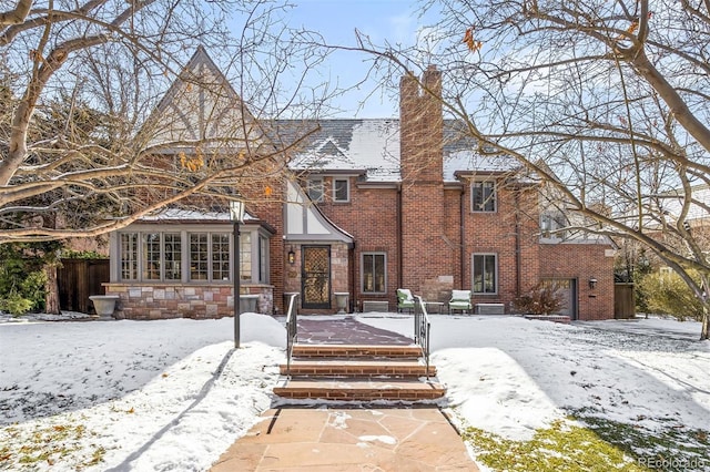 tudor-style house featuring brick siding, a chimney, and fence