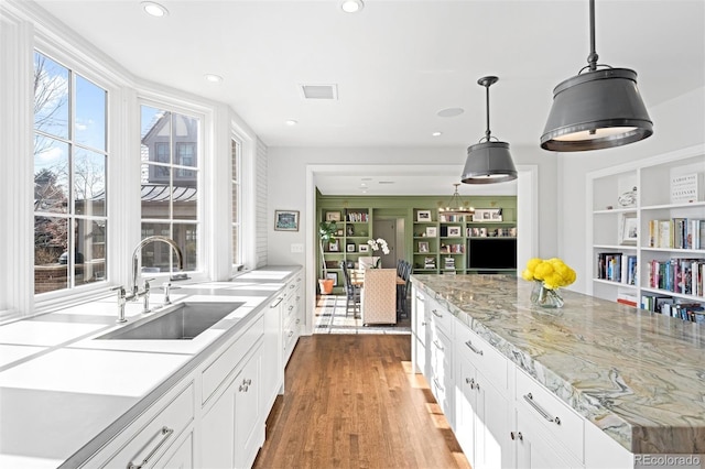 kitchen featuring hanging light fixtures, visible vents, white cabinetry, and a sink