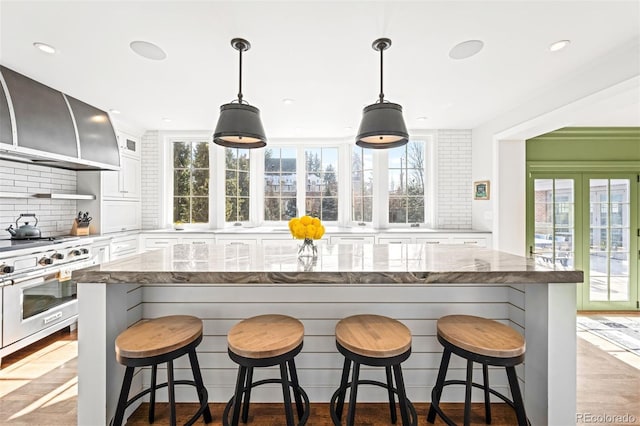 kitchen with wall chimney exhaust hood, white cabinets, a kitchen island, and a kitchen bar