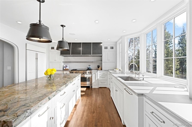 kitchen with a sink, high quality appliances, white cabinetry, hanging light fixtures, and light stone countertops