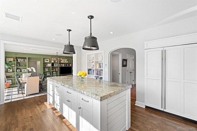 kitchen featuring visible vents, arched walkways, white cabinets, light stone countertops, and pendant lighting