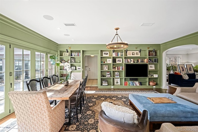 living room with built in shelves, arched walkways, visible vents, and crown molding