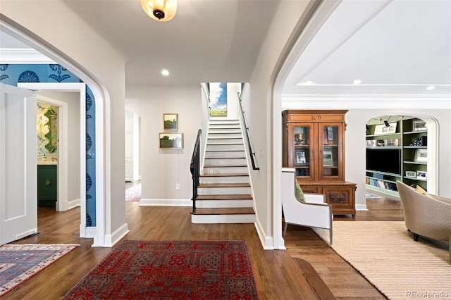 entryway with arched walkways, dark wood finished floors, stairs, crown molding, and recessed lighting