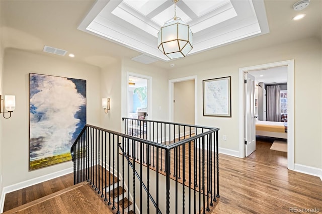 hall with a tray ceiling, visible vents, an upstairs landing, wood finished floors, and baseboards