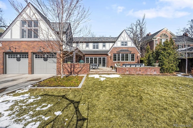 rear view of house with brick siding, a lawn, concrete driveway, an attached garage, and stucco siding