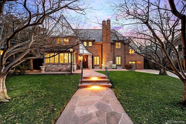 english style home featuring a yard, a patio area, brick siding, and a chimney