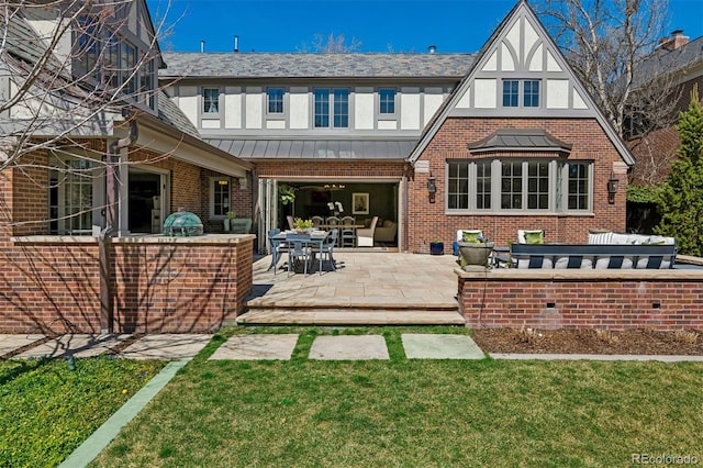 back of house featuring a patio area, brick siding, stucco siding, a lawn, and a standing seam roof