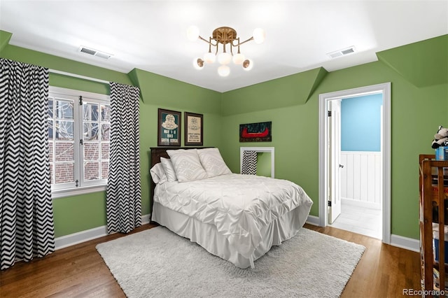 bedroom with visible vents, wood finished floors, baseboards, and a notable chandelier