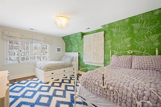 bedroom featuring wallpapered walls, wood finished floors, visible vents, and baseboards