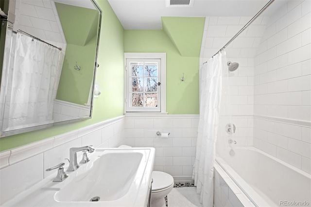 bathroom featuring tiled shower / bath combo, tile walls, toilet, wainscoting, and a sink