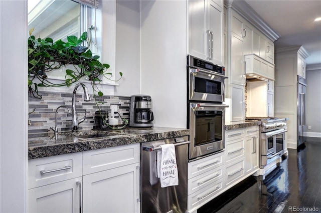 kitchen with appliances with stainless steel finishes, dark stone counters, dark hardwood / wood-style floors, and white cabinets