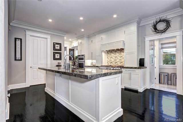 kitchen featuring dark wood-type flooring, dark stone counters, a center island with sink, and white cabinets