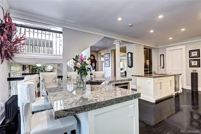 kitchen featuring a large island with sink, dark wood-type flooring, ornamental molding, decorative columns, and white cabinets