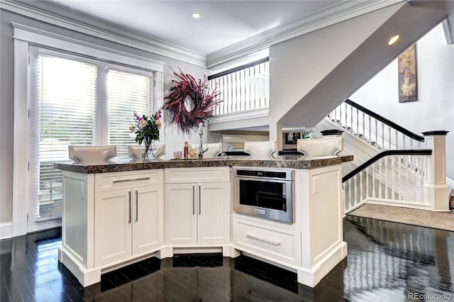 kitchen featuring dark hardwood / wood-style floors, oven, kitchen peninsula, crown molding, and white cabinetry