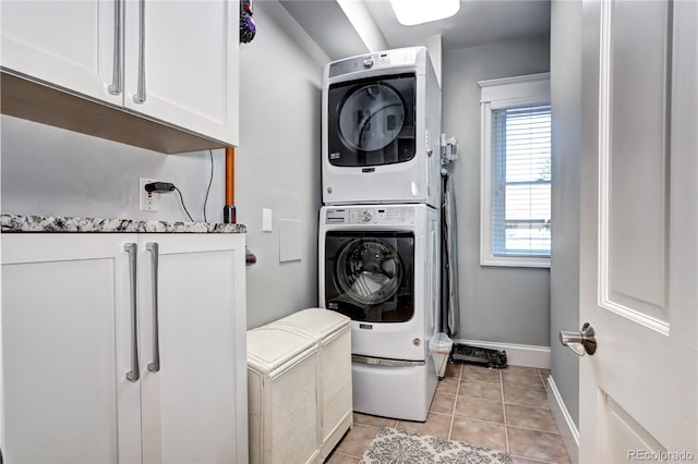 clothes washing area with light tile patterned floors, cabinets, and stacked washer and dryer