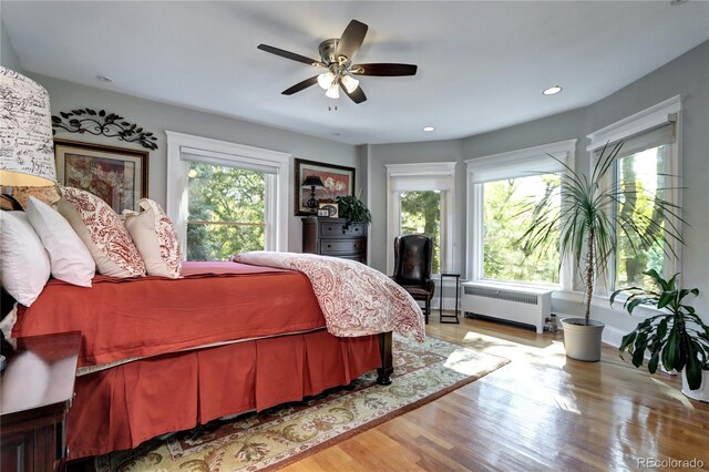 bedroom featuring multiple windows, hardwood / wood-style floors, radiator, and ceiling fan