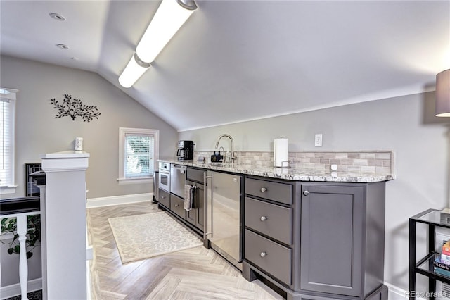 kitchen with lofted ceiling, sink, light stone countertops, gray cabinets, and light parquet flooring