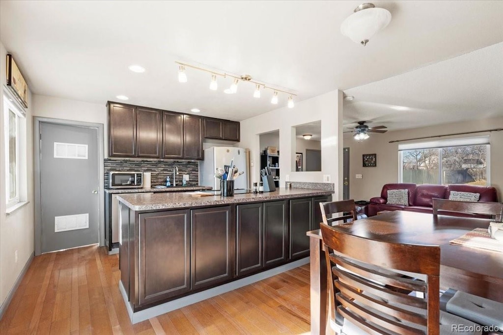 kitchen with light stone countertops, dark brown cabinets, light wood-type flooring, and white refrigerator