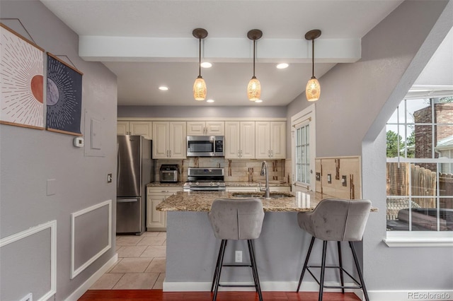 kitchen featuring decorative backsplash, appliances with stainless steel finishes, a sink, a peninsula, and cream cabinetry