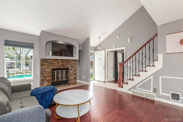 living room featuring visible vents, wood finished floors, a fireplace, stairway, and vaulted ceiling