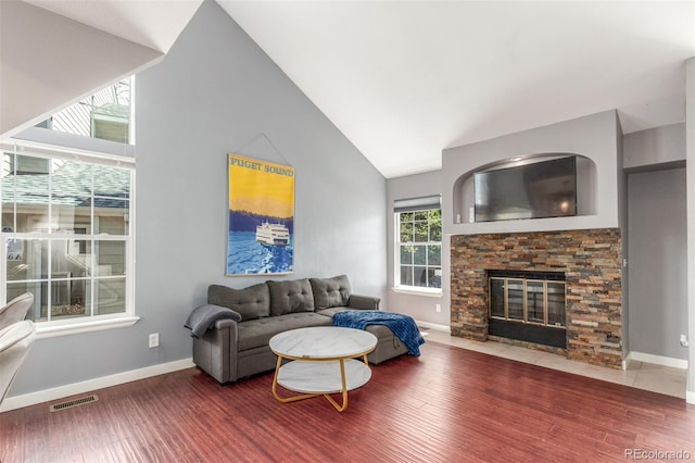 living area with visible vents, a fireplace, wood finished floors, baseboards, and lofted ceiling
