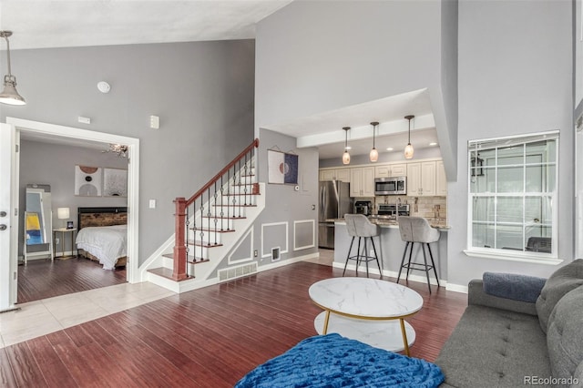 living room featuring visible vents, stairs, wood finished floors, and high vaulted ceiling