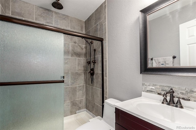bathroom featuring toilet, a textured wall, a shower stall, and vanity