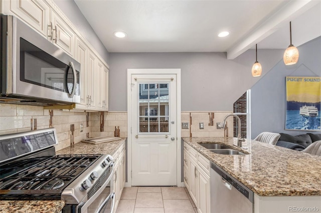 kitchen featuring a peninsula, light tile patterned flooring, light stone countertops, a sink, and appliances with stainless steel finishes