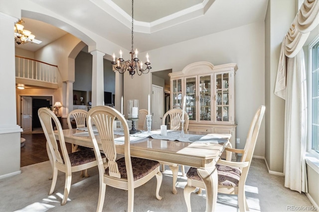 dining space featuring a tray ceiling, decorative columns, light colored carpet, and a chandelier