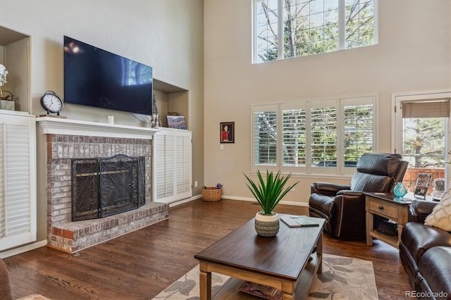 living area featuring a healthy amount of sunlight, a brick fireplace, baseboards, and wood finished floors