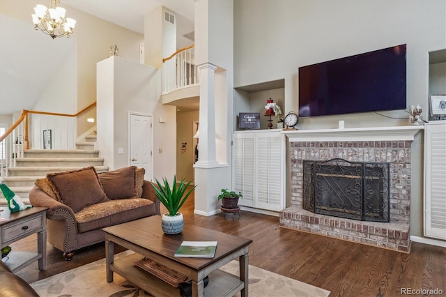 living room featuring visible vents, wood finished floors, decorative columns, a brick fireplace, and stairs